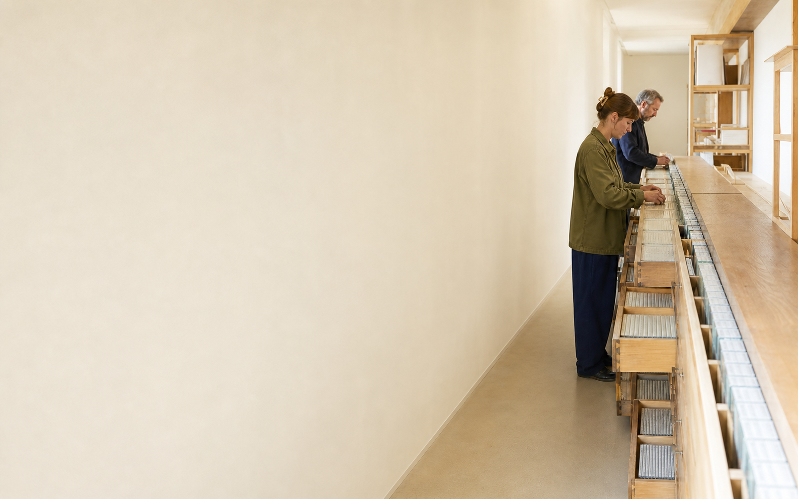 Zwei Menschen sortieren Medienhüllen in langen Archivschubladen eines hellen Korridors