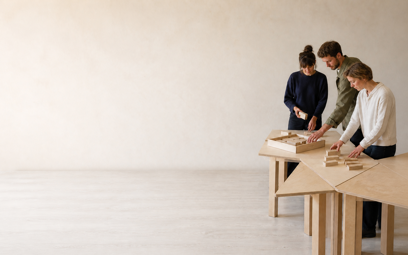 Drei Menschen verteilen Holzbausteine auf verbundenen Arbeitsflächen in einem hellen Studio